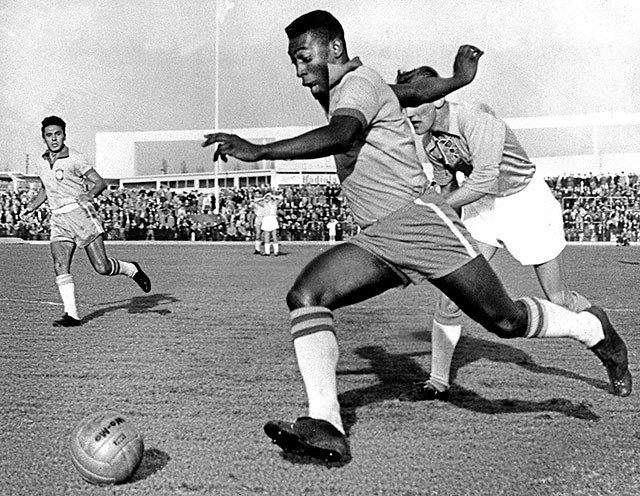 Brazilian football legend Pelé dribbles past two defenders.