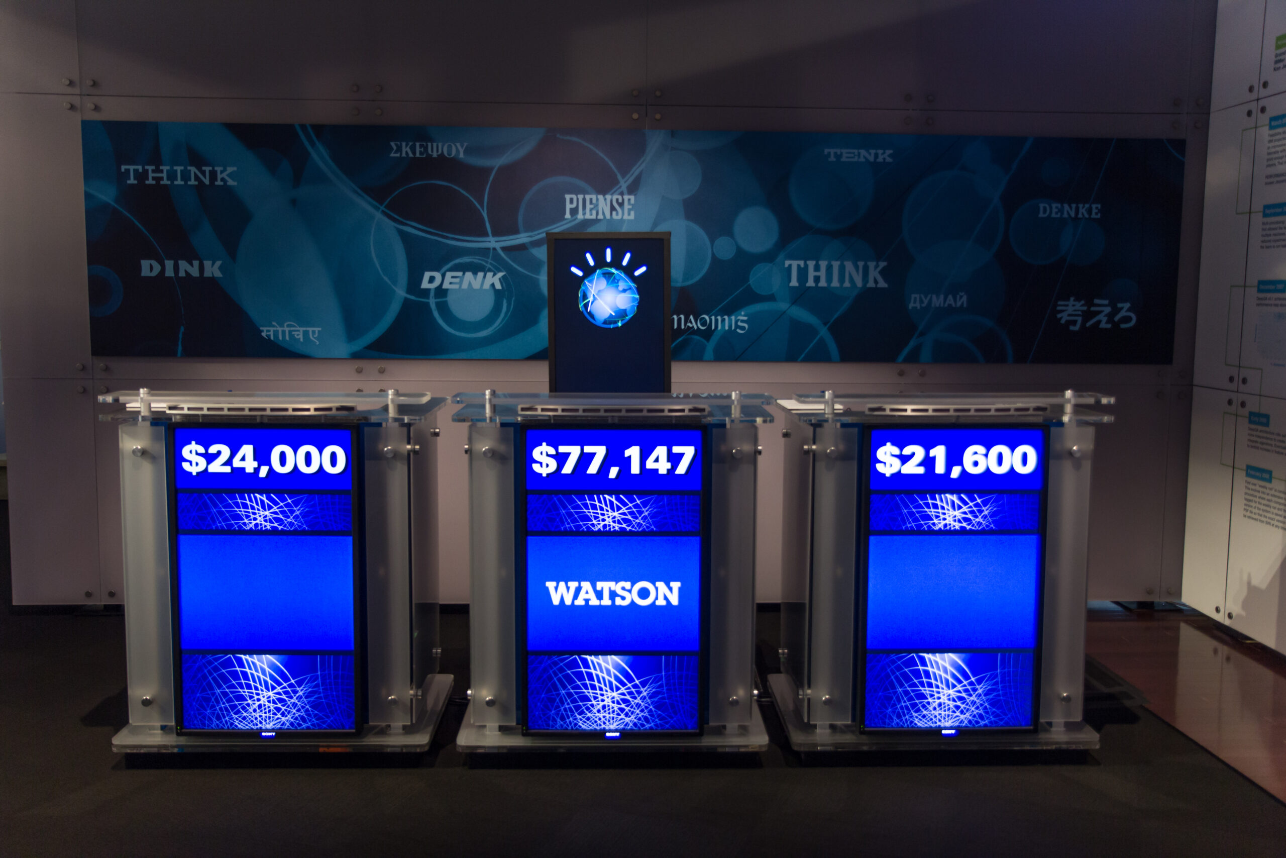An exhibit shows three Jeopardy lecterns with prize winnings displayed. The largest amount belongs to the IBM computer named Watson.