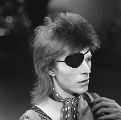 A head shot of David Bowie, looking to his left with an eye patch over his right eye.
