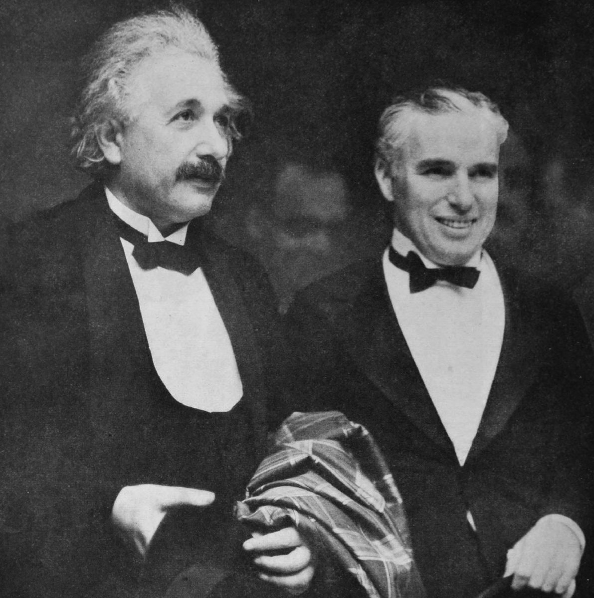 Two men in tuxedos. Albert Einstein with a coat over his left arm, Charlie Chaplin to Einstein's left.